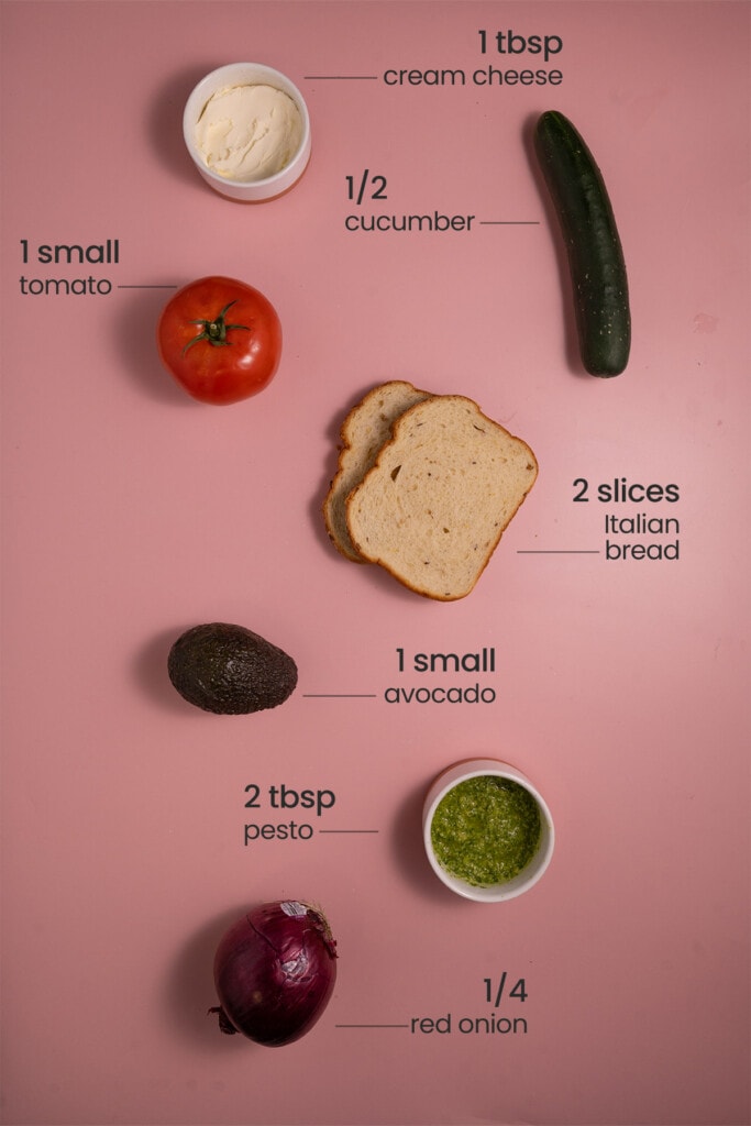 All ingredients for Best Veggie Sandwich including cream cheese, cucumber, tomato, bread, avocado, pesto, and red onion