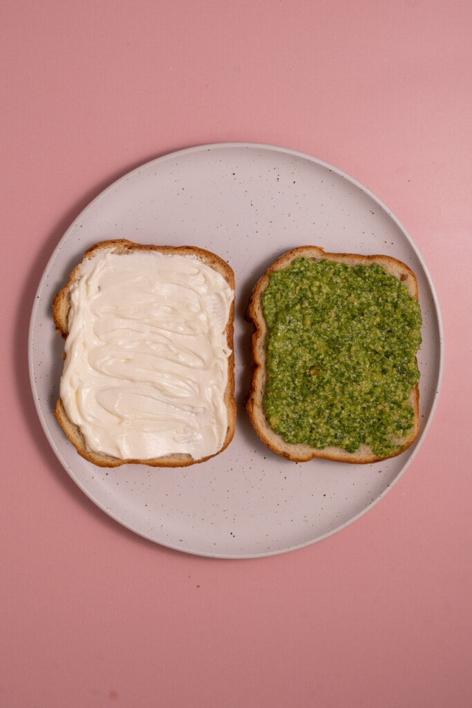 Two slices of bread, one spread with cream cheese and one with pesto