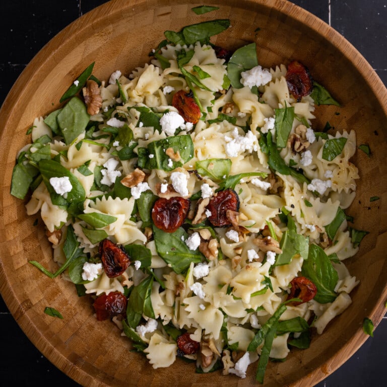 Tossing bow tie pasta with roasted grape tomatoes, spinach, goat cheese, and walnuts