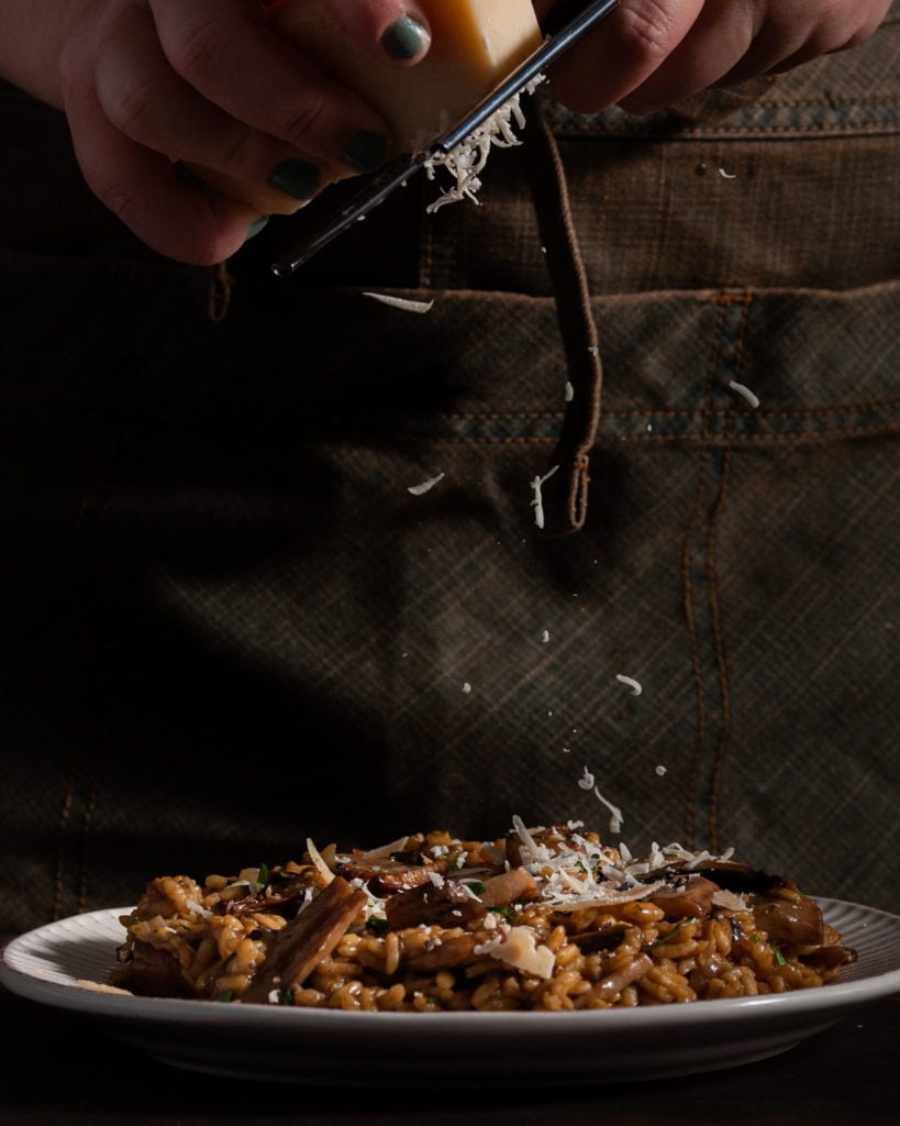 adding shaved parmesan to truffle mushroom risotto