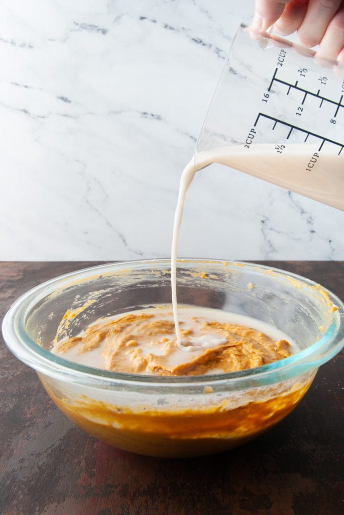 Adding milk to pumpkin muffin batter.