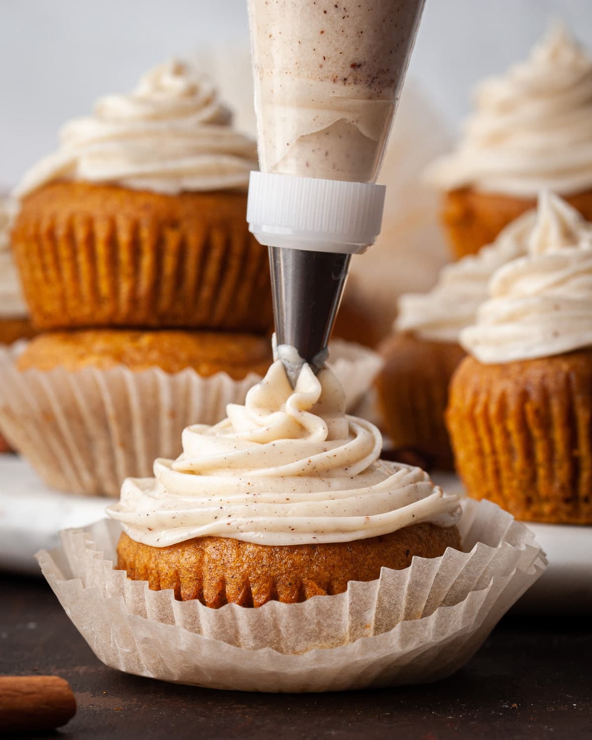 piping spiced cream cheese frosting onto pumpkin muffins