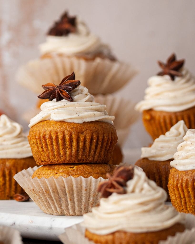 Two pumpkin muffins stacked on top of each other with the top one having cream cheese frosting.