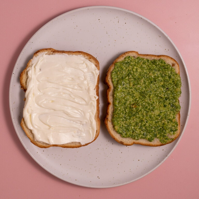 Spreading one slice of bread with cream cheese and one with pesto