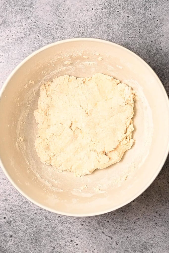 Using hands to bring biscuit dough together in a mixing bowl.