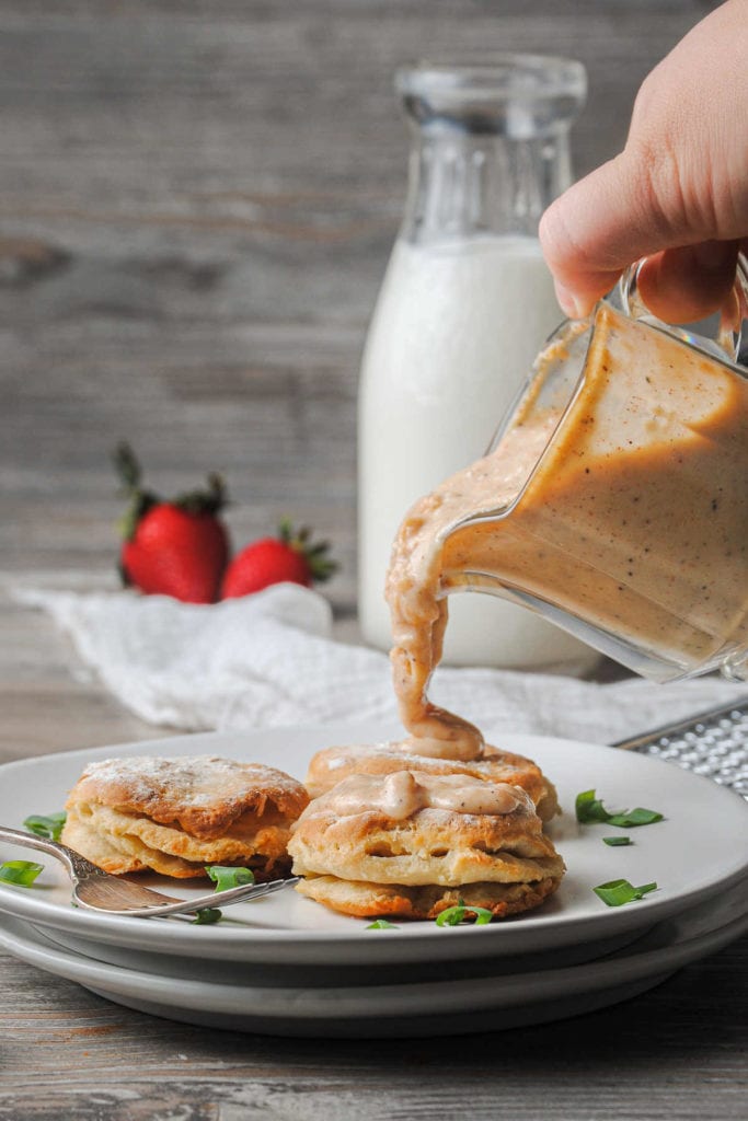 pouring vegetarian gravy over biscuits on a plate with scallions