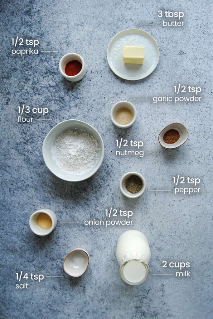 Overhead view of all the ingredients needed for vegetarian gravy for biscuits - paprika, butter, garlic powder, flour, nutmeg, pepper, onion powder, salt, and milk.