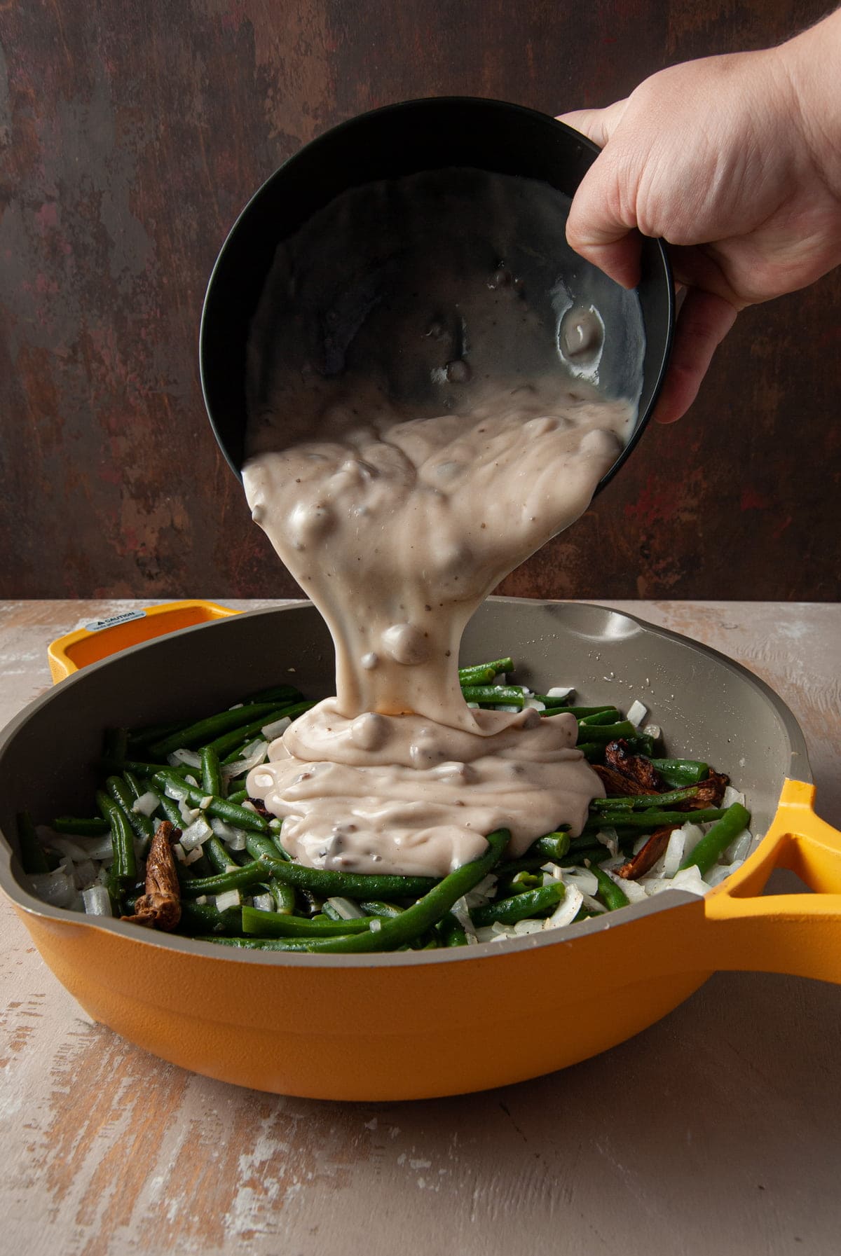 pouring cream of mushroom soup over vegetables cooking in pan