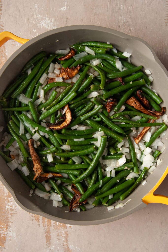 Adding boiled green beans to sauteed garlic, onion, and porcini mushrooms.