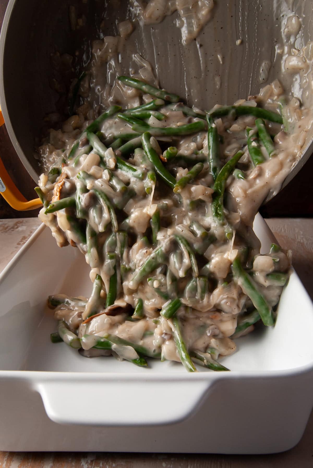 pouring cooked green bean casserole with secret ingredient components into a baking dish