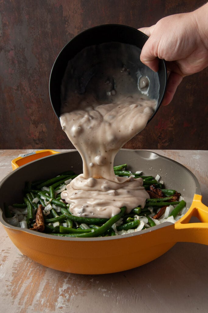 Adding cream of mushroom soup to cooked green beans and other veggies.
