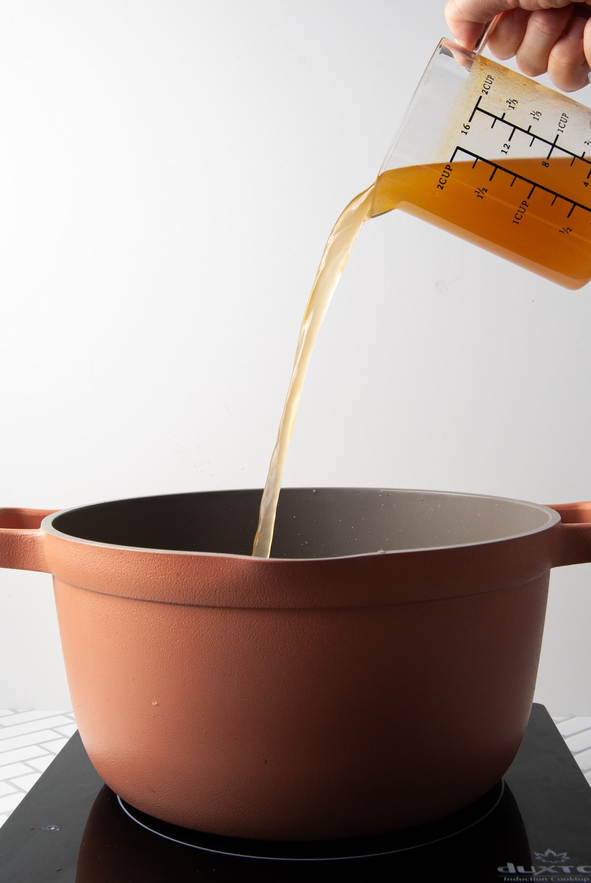 adding veggie broth to a pot