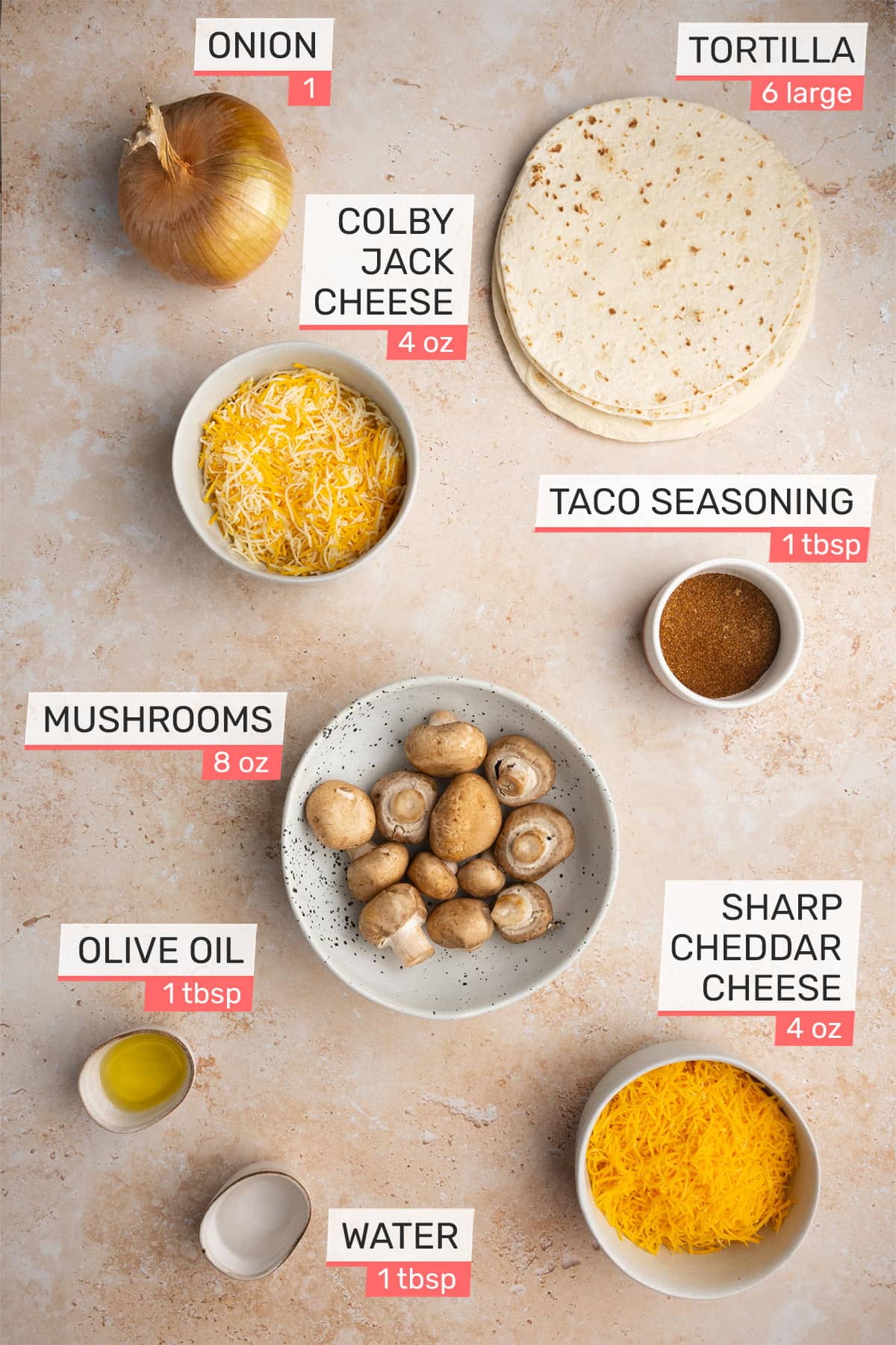 Overhead picture of all ingredients needed for Meatless Enchiladas - Onion, Colby Jack Cheese, Tortilla, Taco Seasoning, Mushrooms, Sharp Cheddar Cheese, Olive Oil, Water