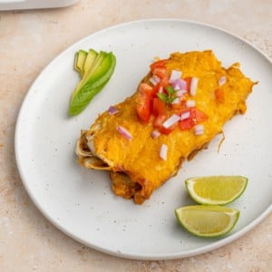 two meatless enchiladas on a plate with lime wedges and sliced avocado
