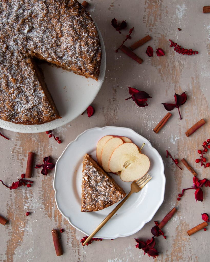 white plate with slice of apple cake next to whole cake on  a white cake stand