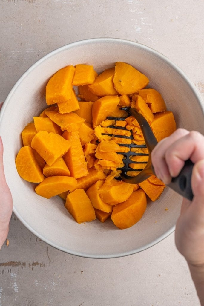 using a potato masher to break down sweet potato