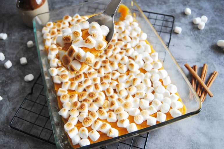 Baking dish full of Maple Sweet Potato Casserole with a serving spoon scooping a spoonful out