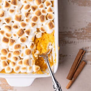 Maple sweet potato casserole topped with toasted marshmallows with a serving taken out and a spoon in it.