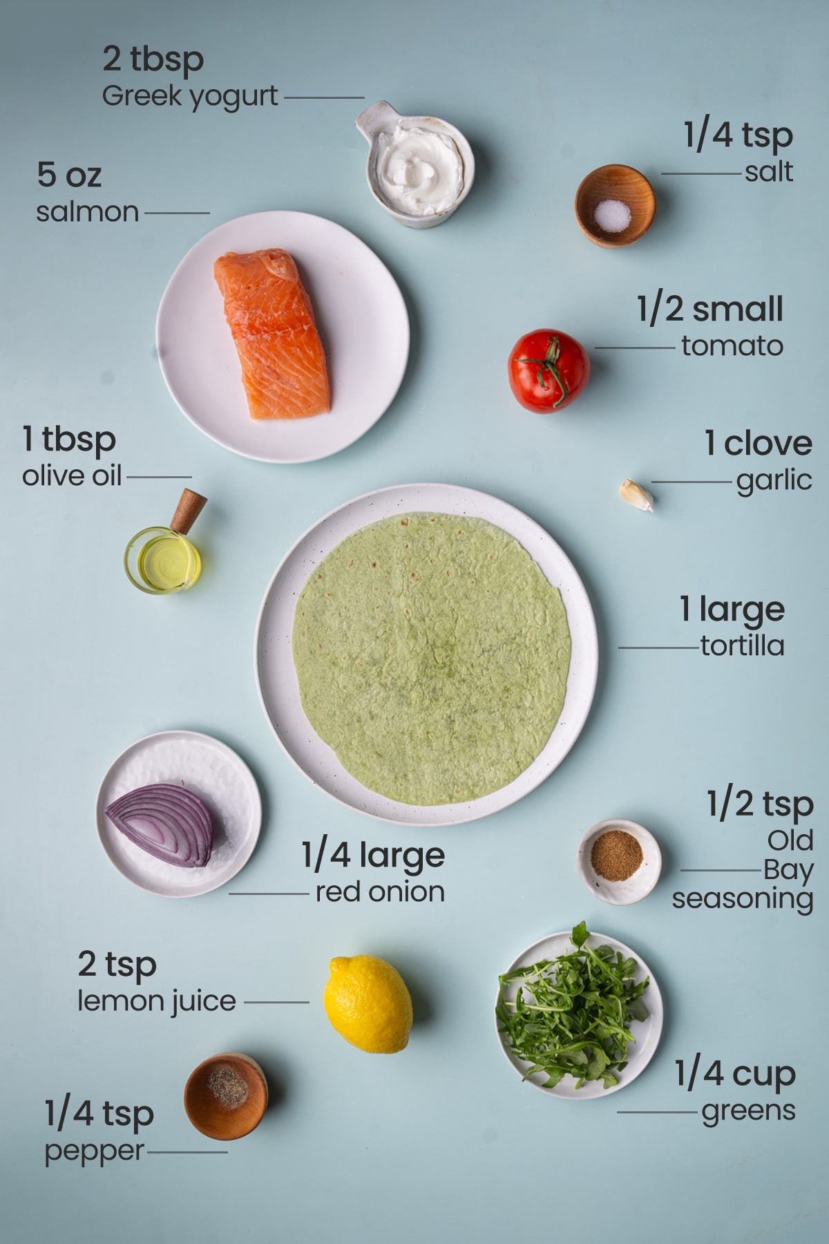 All ingredients needed for a Salmon Wrap including Greek yogurt, salt, salmon, tomato, olive oil, wrap, red onion, Old Bay seasoning, arugula, lemon, and pepper.