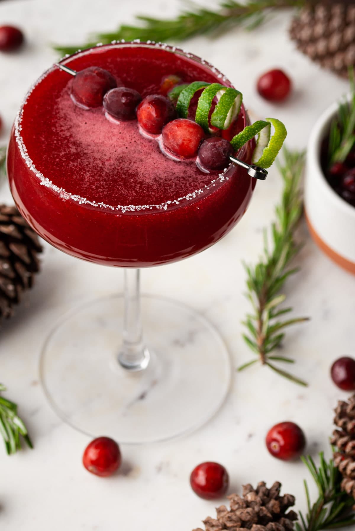 cranberry cosmo garnished with whole cranberries and twisted zested lime