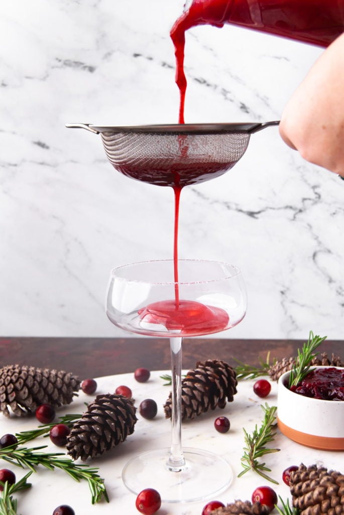 pouring cranberry cosmo through a sieve