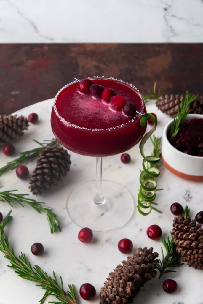 leftover cranberry sauce cosmo surrounded by pine cones, rosemary, and fresh cranberries