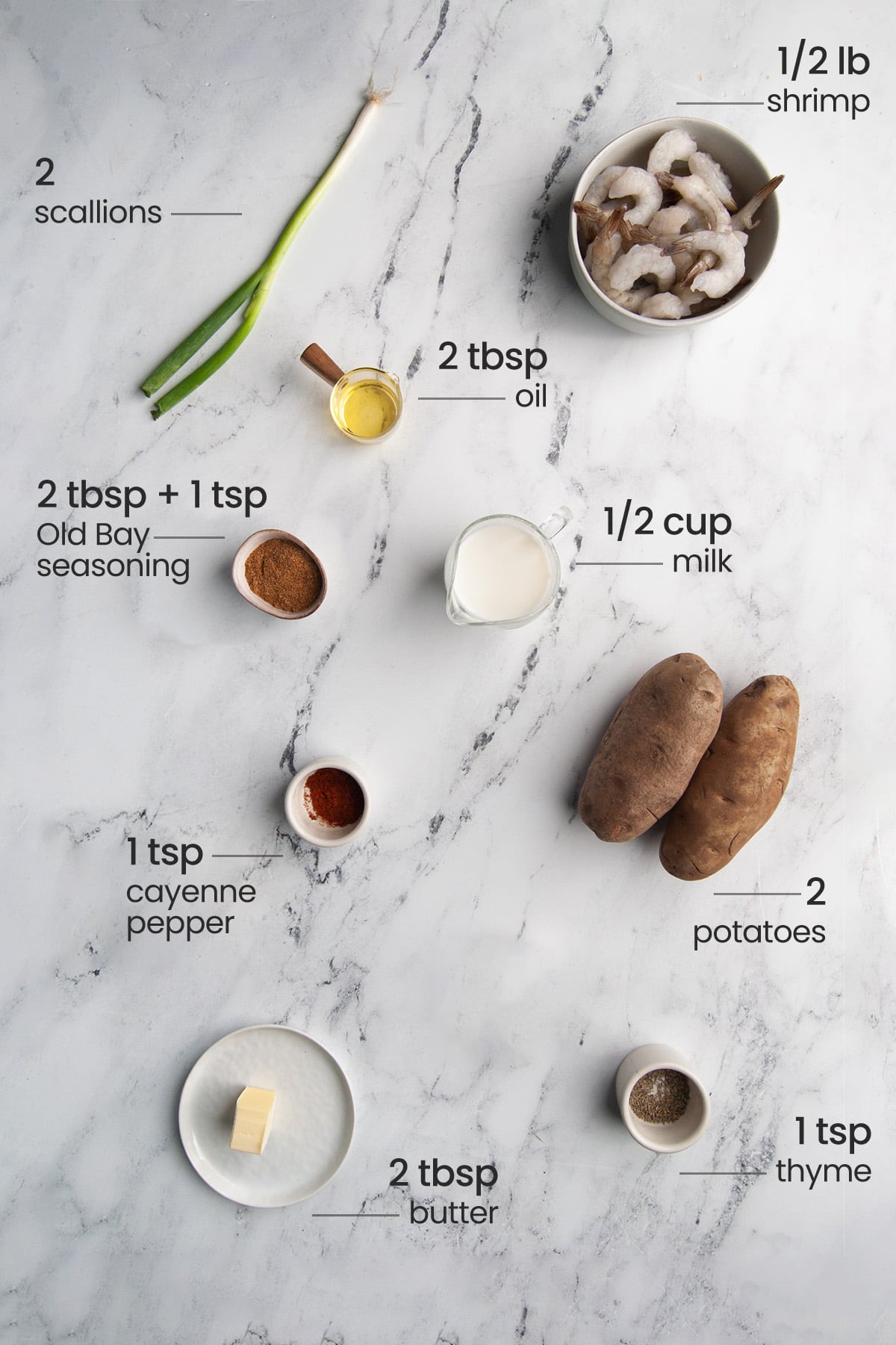 Overhead view of the ingredients needed for blackened shrimp with Old Bay mashed potatoes - shrimp, scallions, oil, Old Bay seasoning, milk, cayenne pepper, potatoes, butter, and thyme.