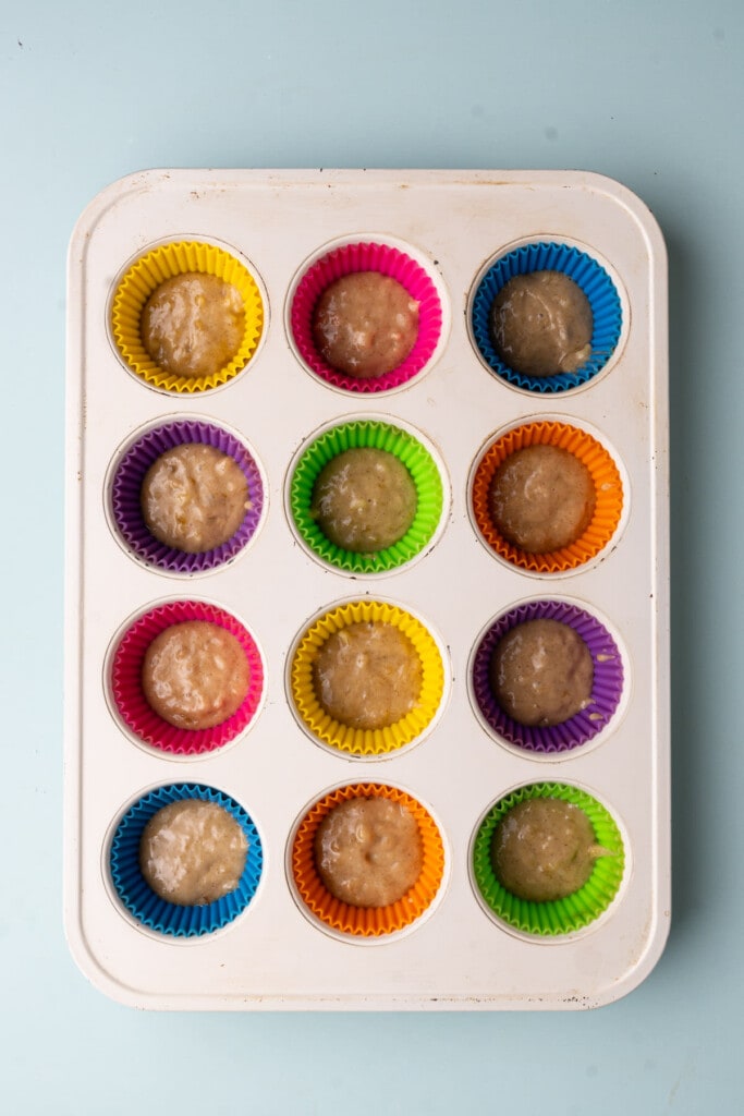 Muffin tin lined with reusable liners with 1 tablespoon of banana muffin batter at the bottom of each. 