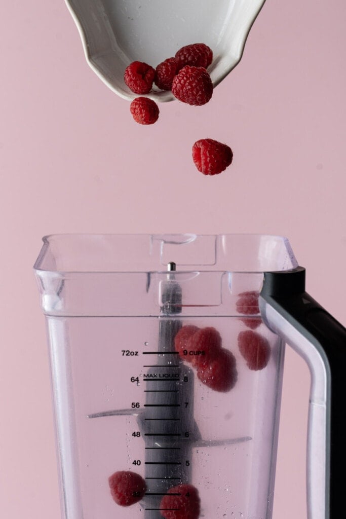Adding raspberries to a blender.