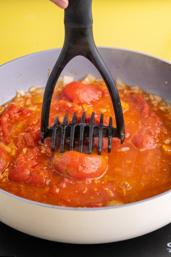 Using a potato masher to crush whole canned tomatoes