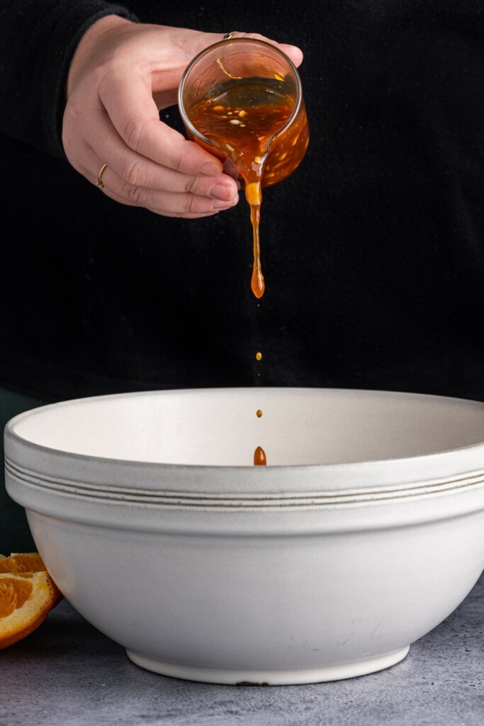 Pouring sticky orange sauce over tofu to toss and coat