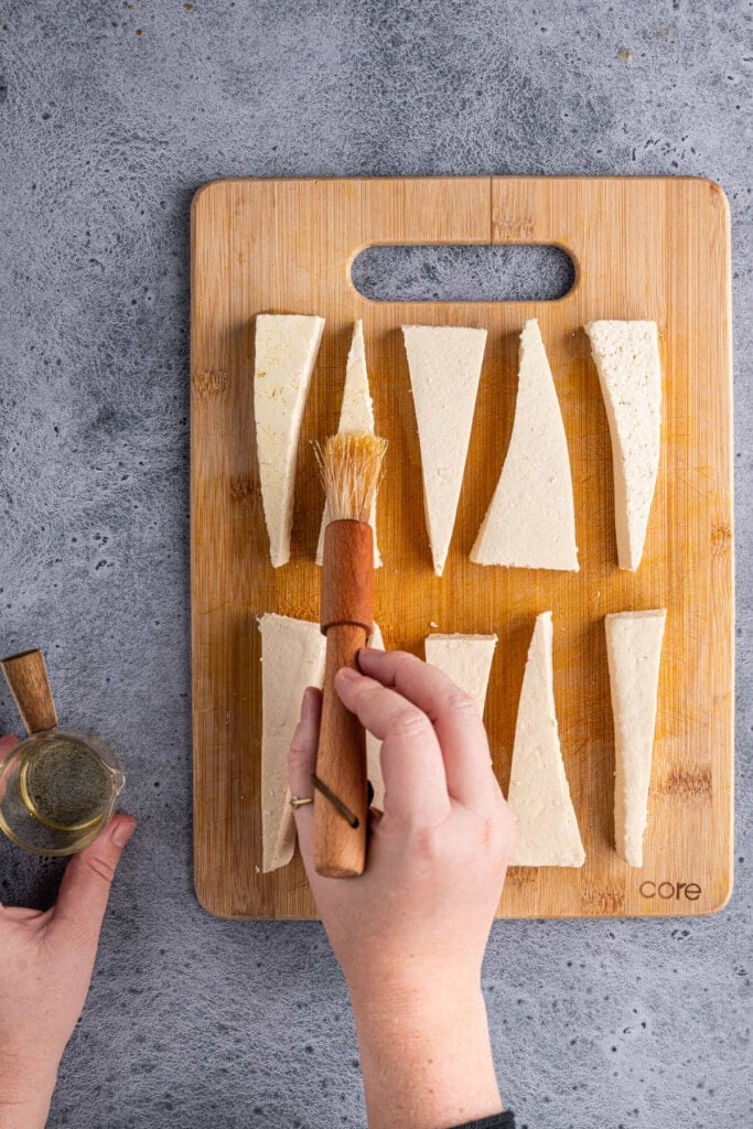 Using a pastry brush to evenly apply oil to tofu