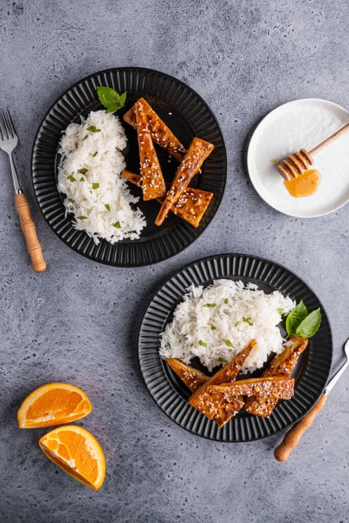 Overhead shot of two plates of orange tofu with white rice