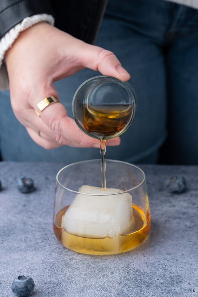 Pouring whiskey over a big block of whiskey ice in a lowball glass. 