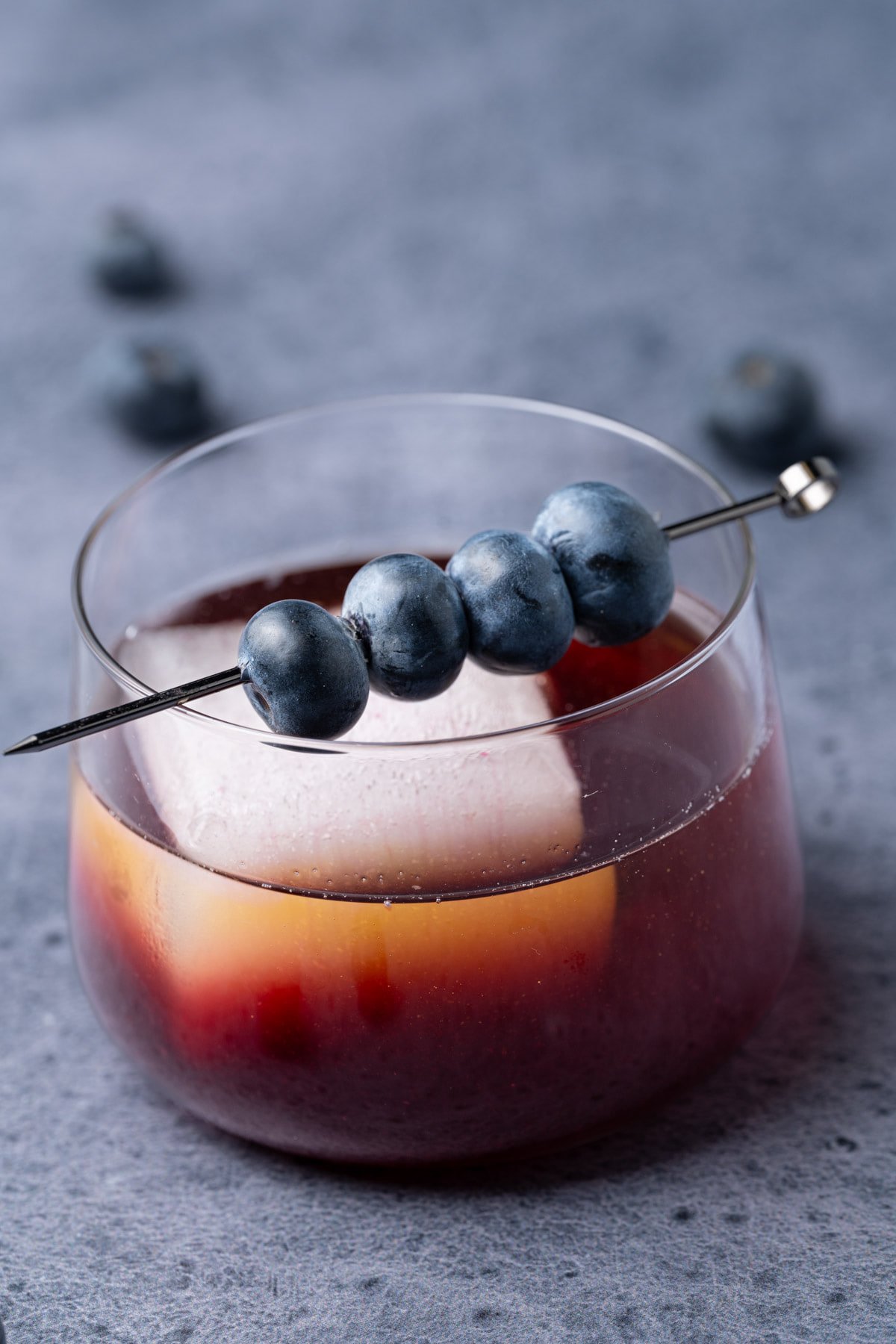 Close up of a blueberry Old Fashioned in a lowball glass garnished with fresh blueberries. 