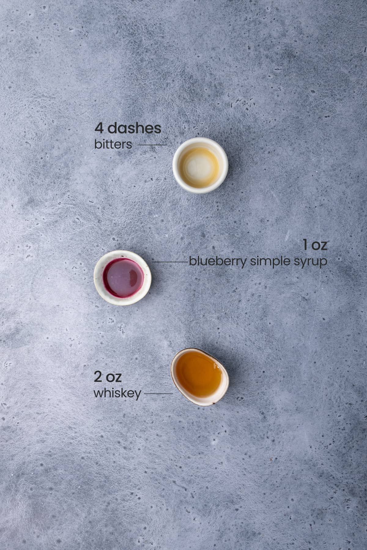Overhead view of ingredients needed for Whiskey Blues Cocktail - bitters, blueberry simple syrup, and whiskey.