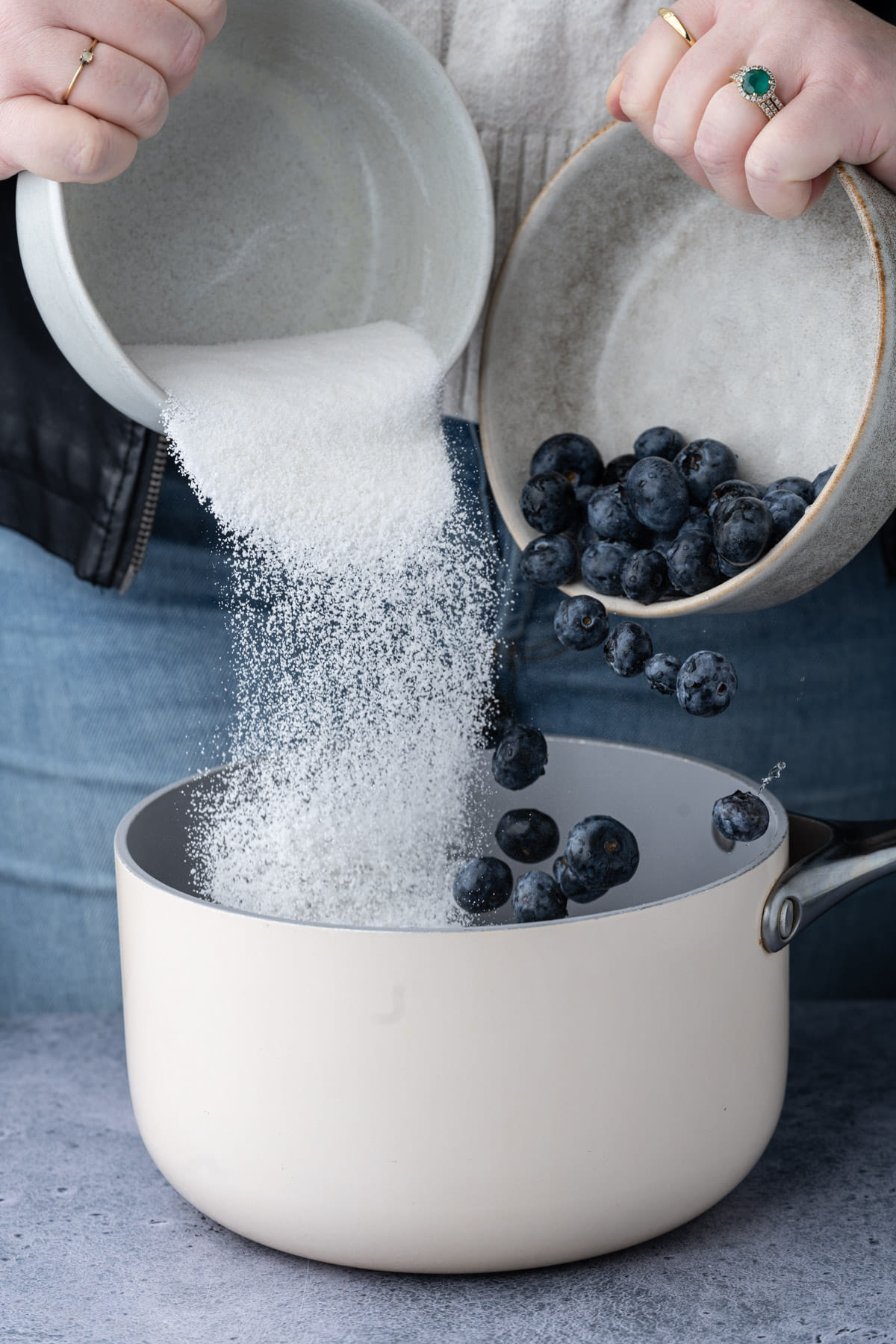 Adding granulated sugar and fresh blueberries to a pot with water to boil. 
