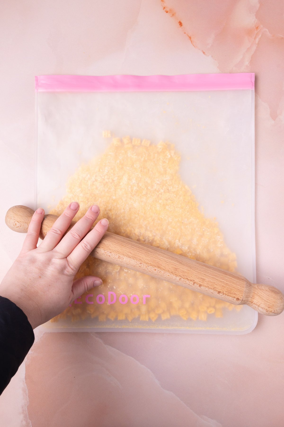 Using a rolling pin to crush cereal in a large reusable storage bag. 