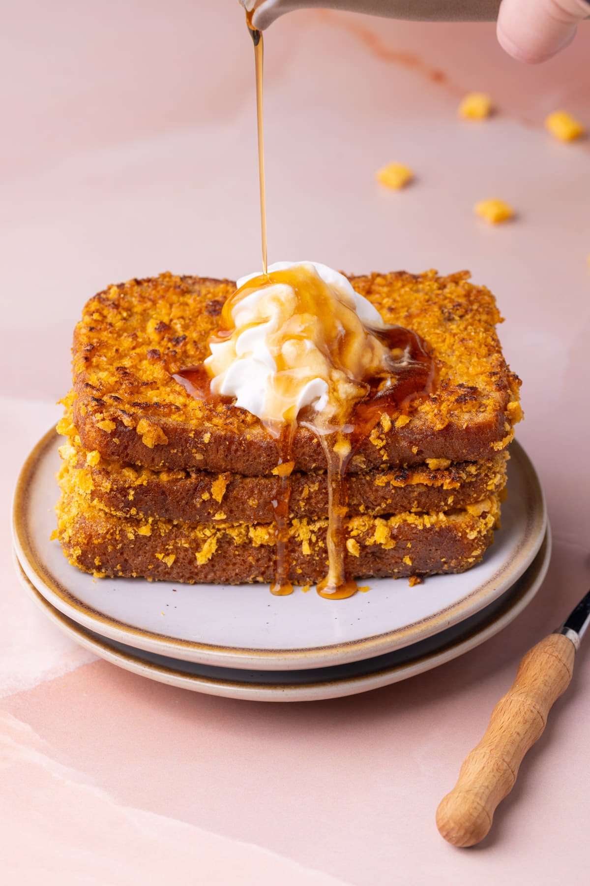 Pouring maple syrup over French toast coated in Captain Crunch cereal garnished with whipped cream.