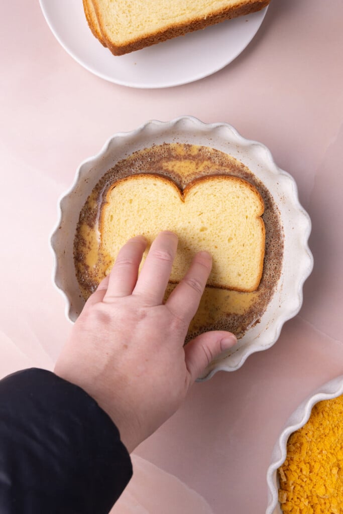 Dunking a slice of brioche into the egg wash.