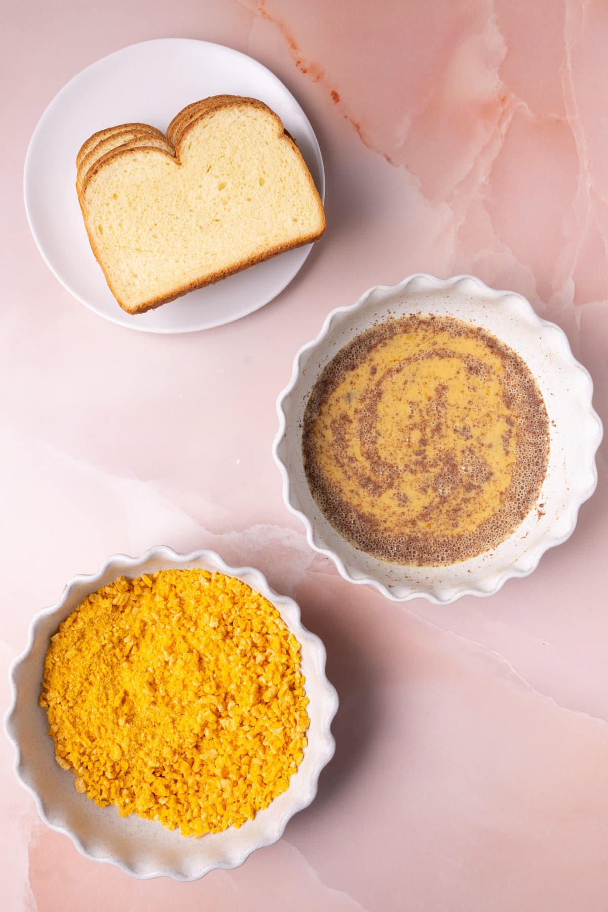 Bread, egg wash, and crushed Captain Crunch set up in an assembly line. 