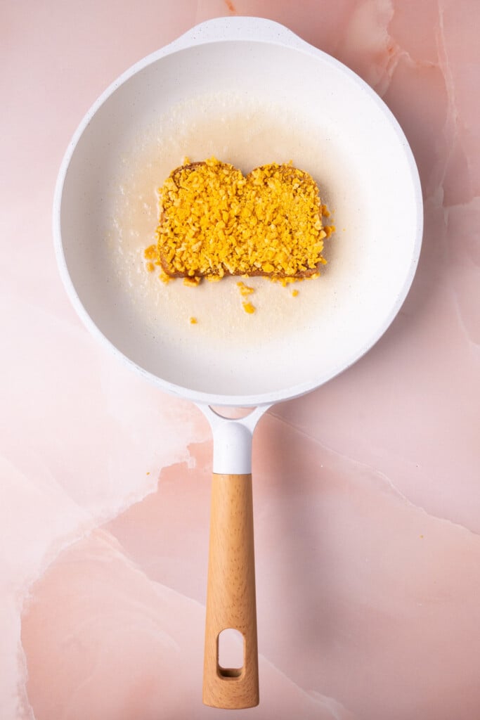 Placing Captain Crunch coated French toast into hot butter in a pan to fry. 