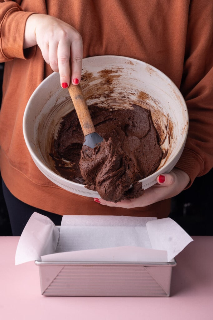 Adding brownie batter to a lined baking dish. 