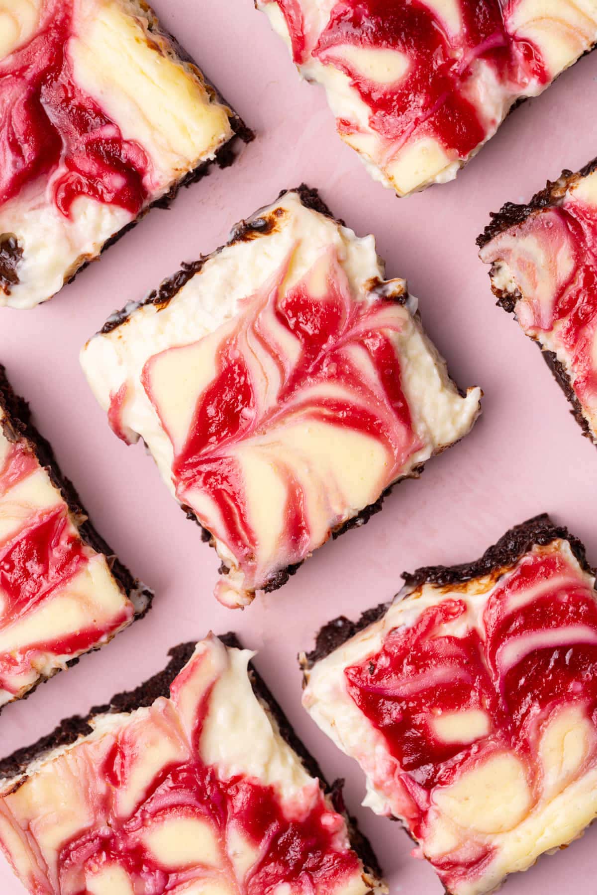 Overhead image of Raspberry Cheesecake Brownies lined up on a pink background. 