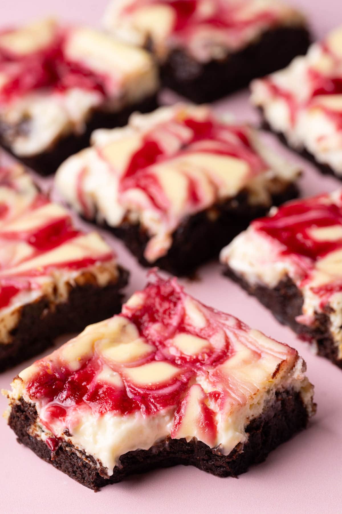 Raspberry Cheesecake Brownies laid out with a bite taken out of the front one. 