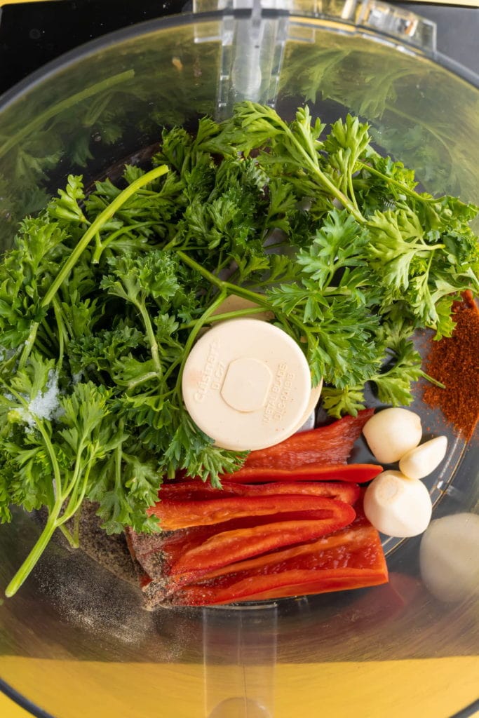 Ingredients for Serrano Pepper Chimichurri - red wine vinegar, fresh parsley, pepper, salt, garlic, serrano peppers, and paprika - in a blender (before blending).