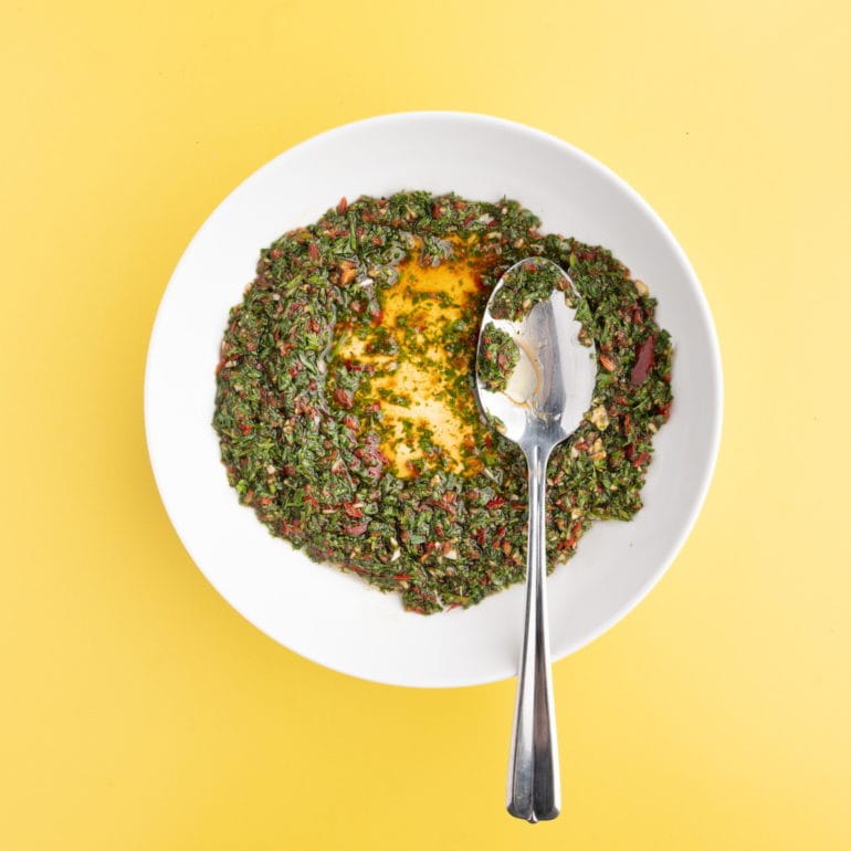 serrano chimichurri in a bowl with a spoon on a yellow background
