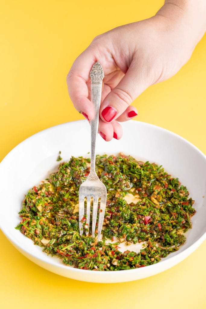 stirring olive oil into chimichurri to make sauce