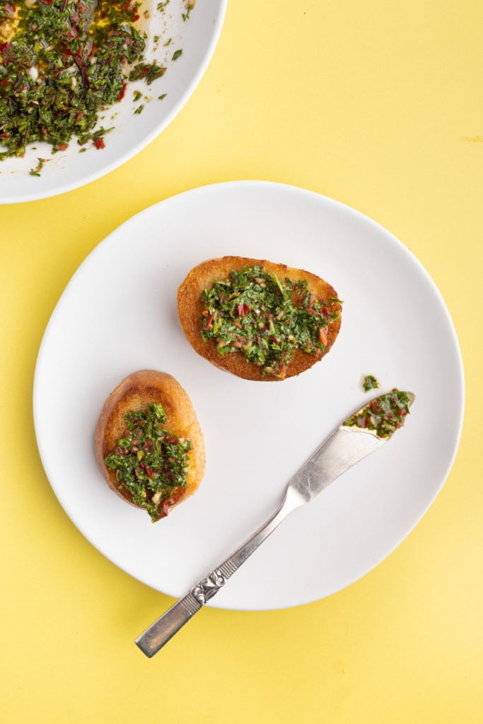 serrano pepper chimichurri spread on 2 pieces of crostini on a white plate