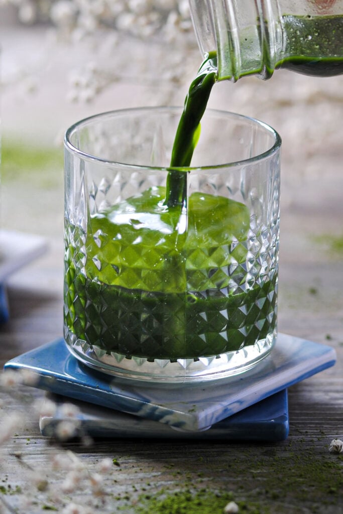 Pouring iced matcha mixed with vodka into a lowball glass with whiskey ice.